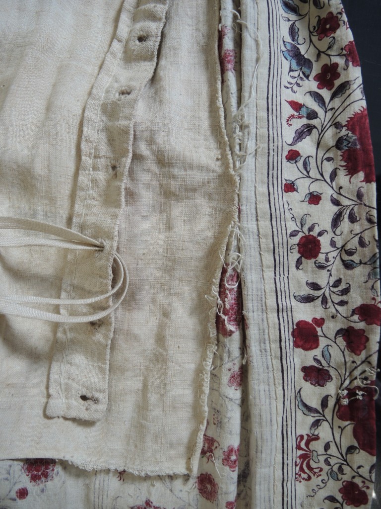 The frayed edge of bodice lining which is detached from the printed fabric, before conservation