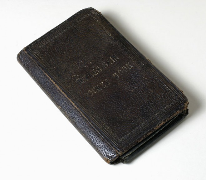 Dark brown pocketbook made of William Burke's tanned human skin on a white surface.