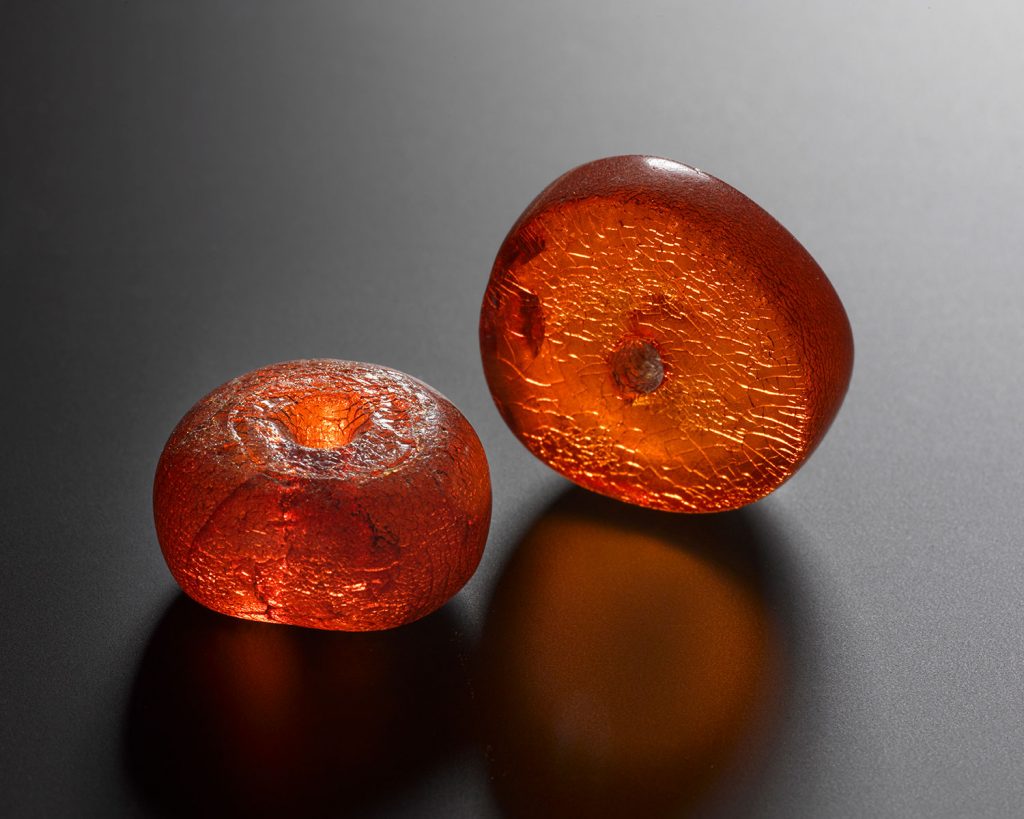 Two circular red-orange Bronze Age amber beads. Look a lot like gummy candies and seeming to pulse with light.