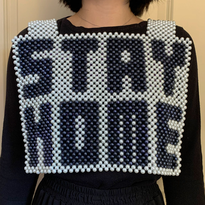 A beaded vest being worn that says "STAY HOME" in black on white.