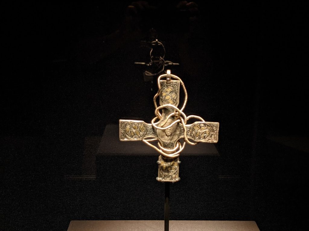 A silver cross with gold details and a chord wrapped around it, appearing to float against a black background.