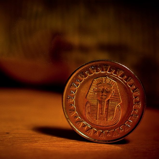 A small brownish-red coin with a pharaoh in the centre set on a wooden table.