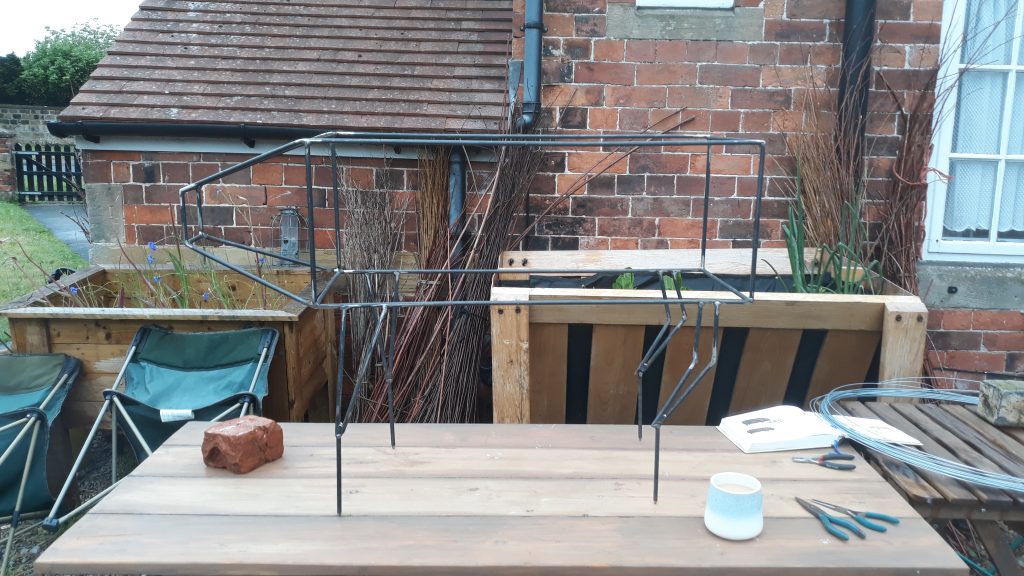 Colour photo of a steel frame of an animal on a workbench in the foreground with a brick wall to a building in the background.