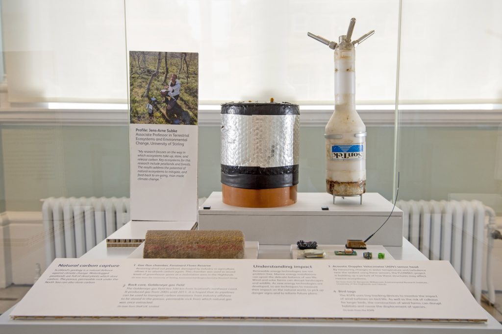 A display case with various objects relating to climate change, like equipment, batteries and testing materials.