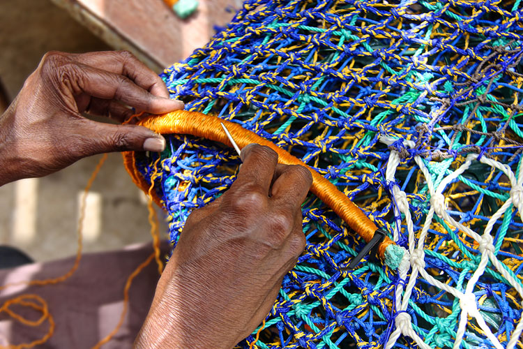 Close-up of two seasoned hands working with a small, sharp tool on a bundled blue plastic net.