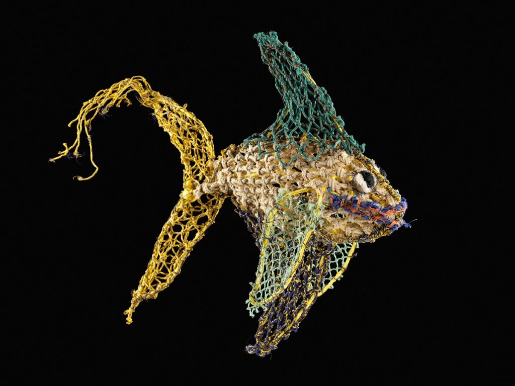An angelfish made from yellow, green, white and blue plastic netting against a black background.
