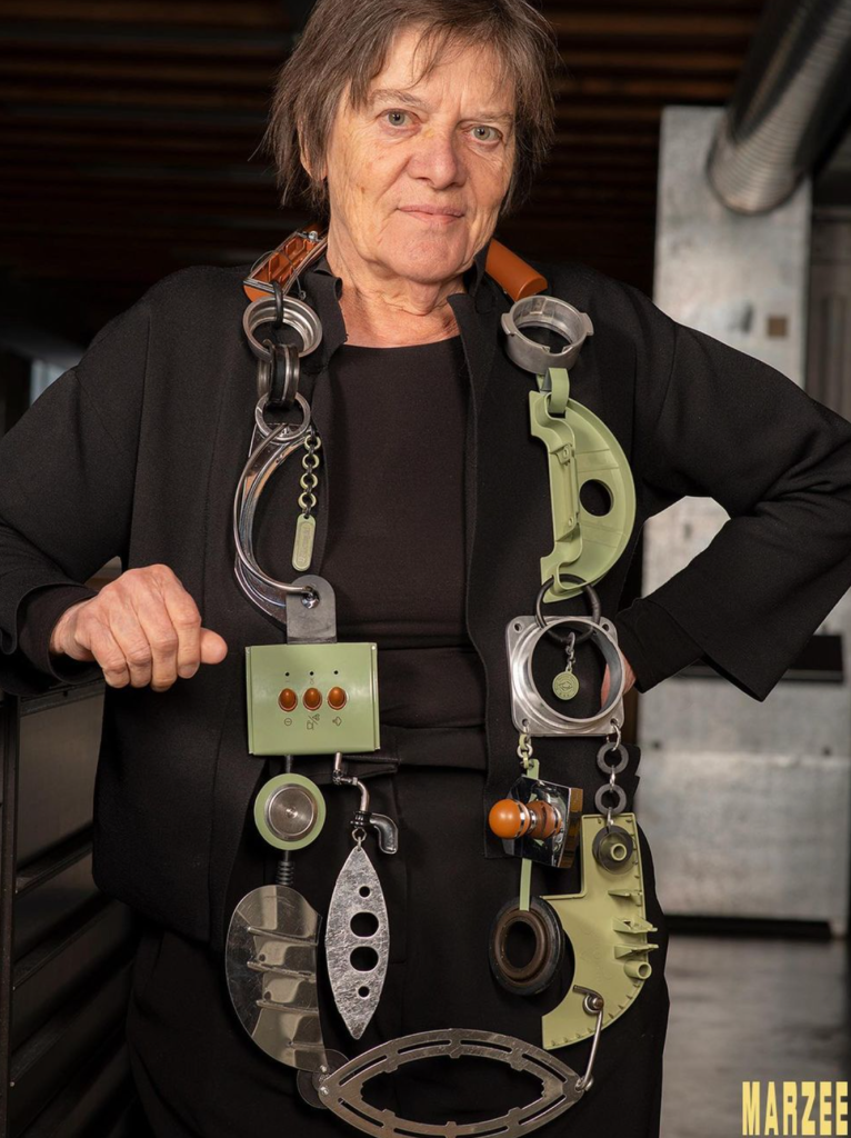 A woman wearing a necklace made of coffee machine parts. The necklace is big and chunky and hangs to below her waist.
