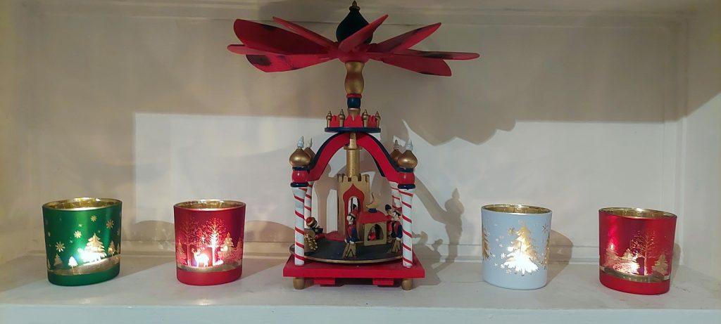 A white shelf containing four candles, each with Christmas tree decorations, and a central pyramid candle with candy cane colouring.