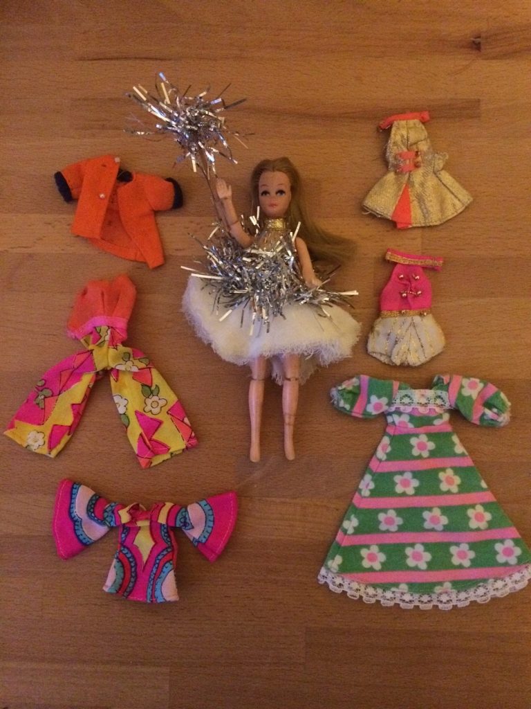 A Pippa doll holding up a foil star, with silver tinsel attached and surrounded by various doll dresses and accessories.