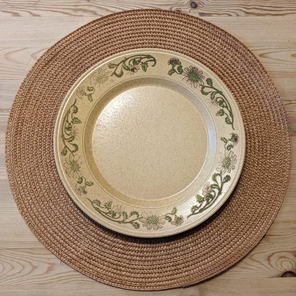 Yellow plate with faded green floral designs around its rim, placed on a light brown placemat on a wooden table.