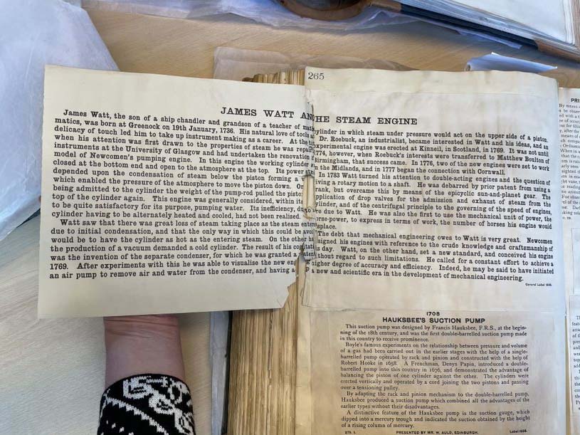 Colour photo of a large book with cream printed labels pasted inside describing the James Watt and the Steam Engine.