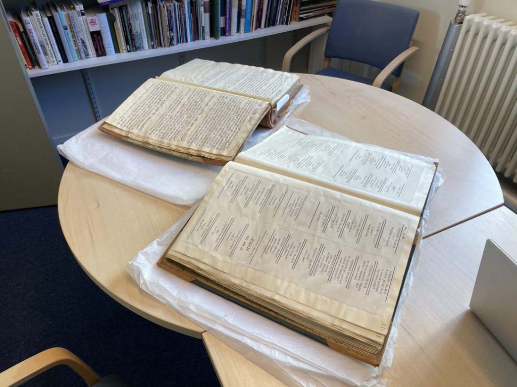 Colour photo of two large open books on a round desk in an office.