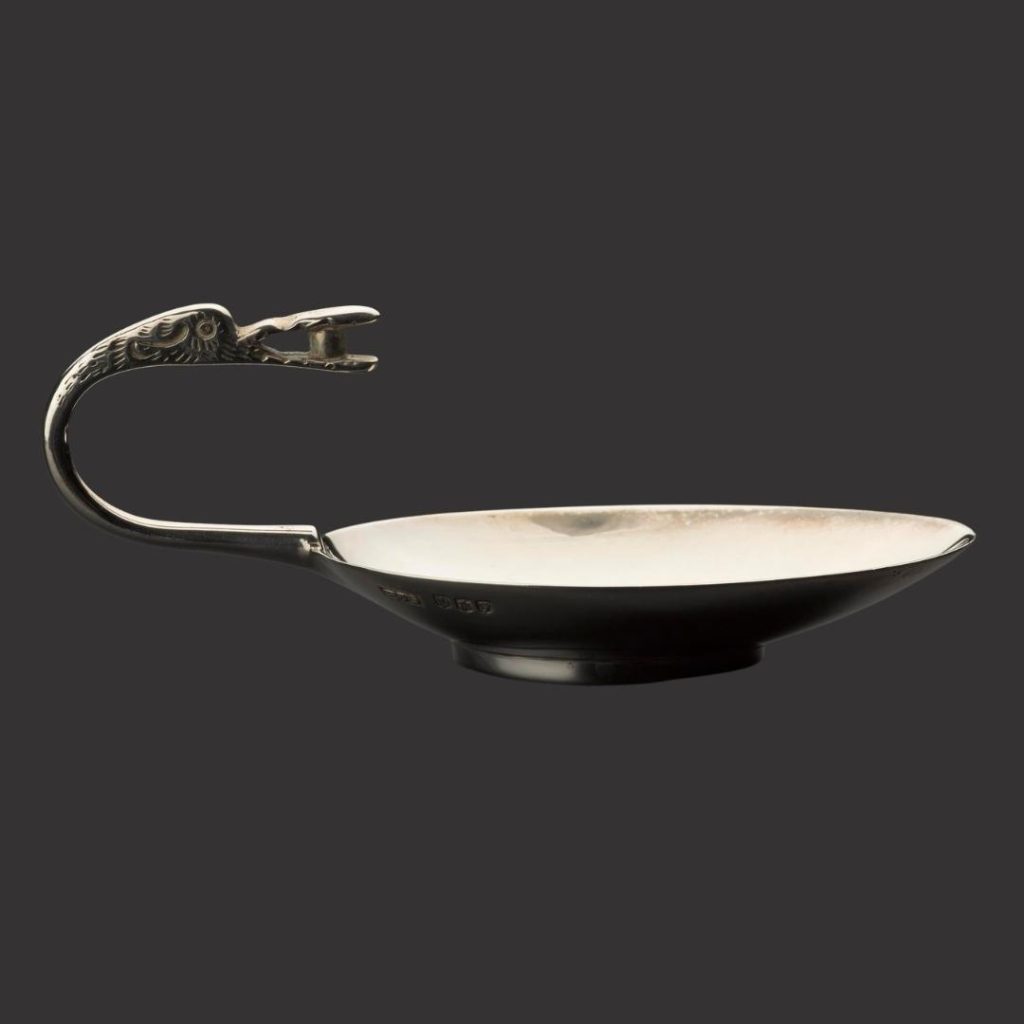 One dark silver spoon, very wide and deep like a little saucer. Its handle curves over the spoon, with a long beaked bird eating a silver berry.