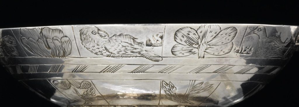 Close up detail of the side of a silver quaich, showing carvings of flowers alternating with birds of varying sizes and poses.
