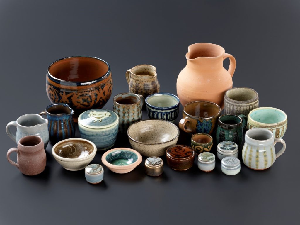 Around two dozen pots of various sizes and colours, from tiny and light blue to large and brown, arranged on a dark grey surface.
