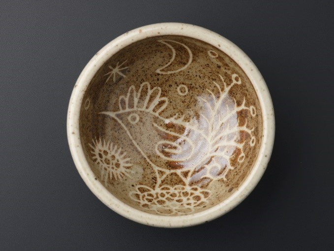 A single pot viewed from straight above. Its bottom has a cartoon-style, peacock-like bird with a moon, stars, and flowers.