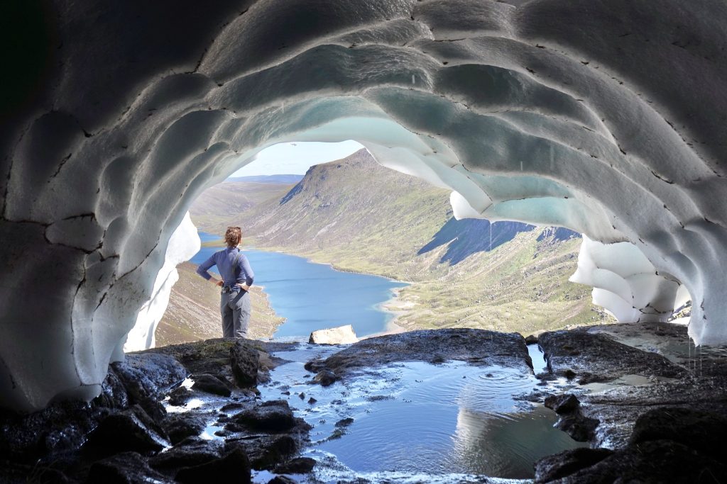 A woman posing in front of Scottish mountains, seen through a snow tunnel.