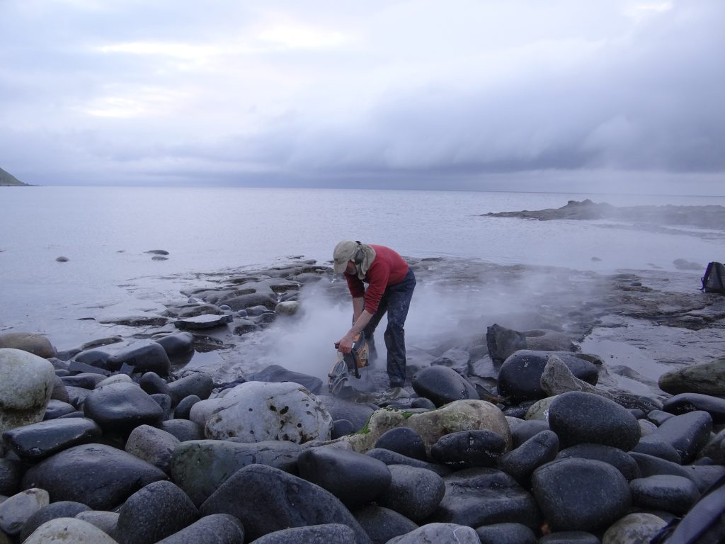 A man using a rock saw on the beach.