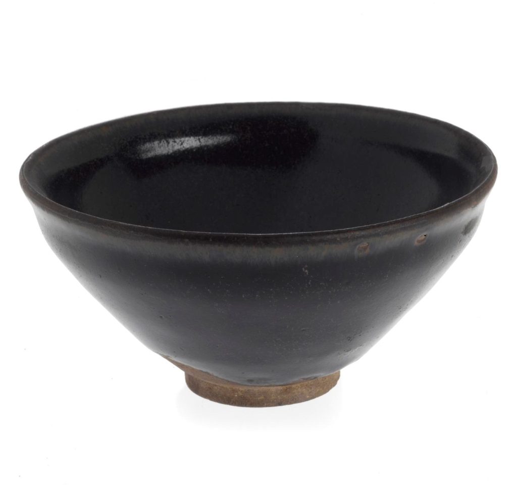 Small, deep bowl wide at the top and tapering towards the bottom. Black or very dark brown in colour against a white background.