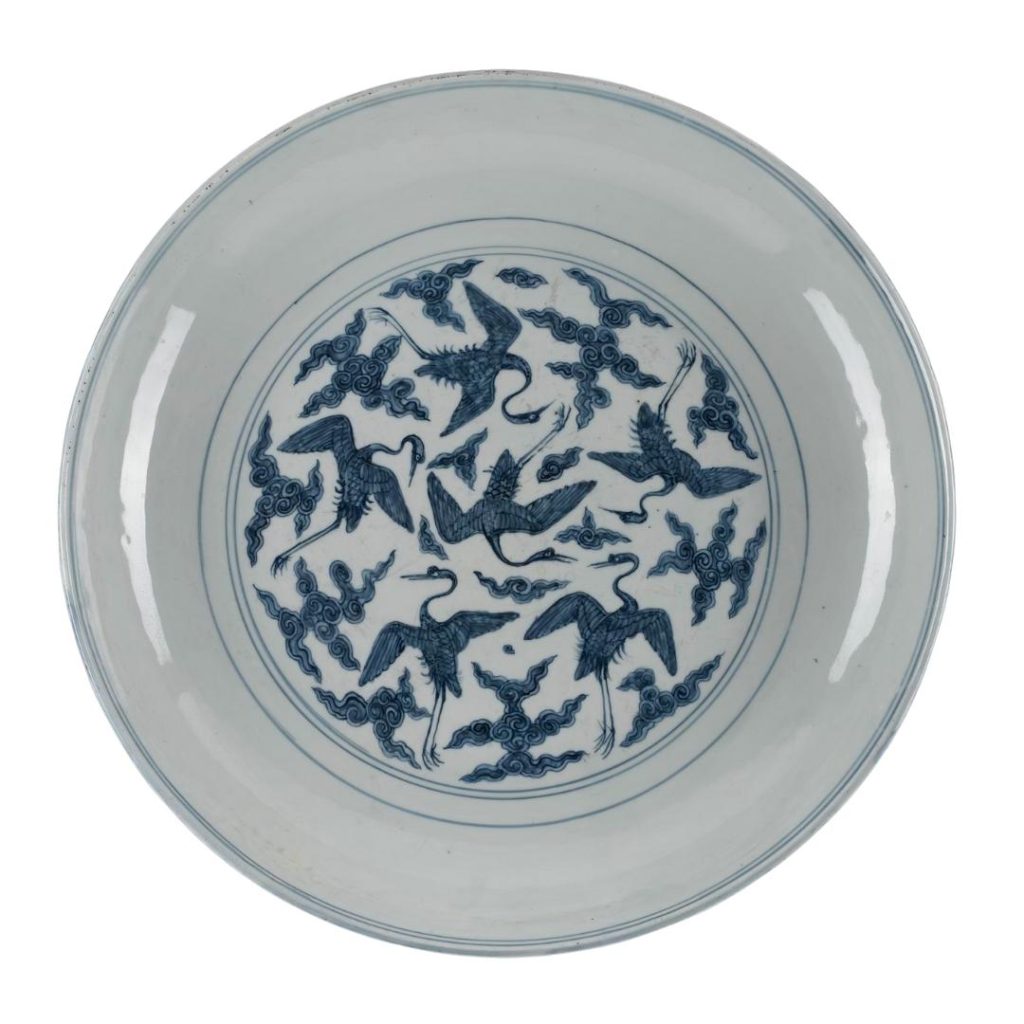 Round blue and white plate with thin blue lines framing a geometric design with six cranes and cloud-like swirls.
