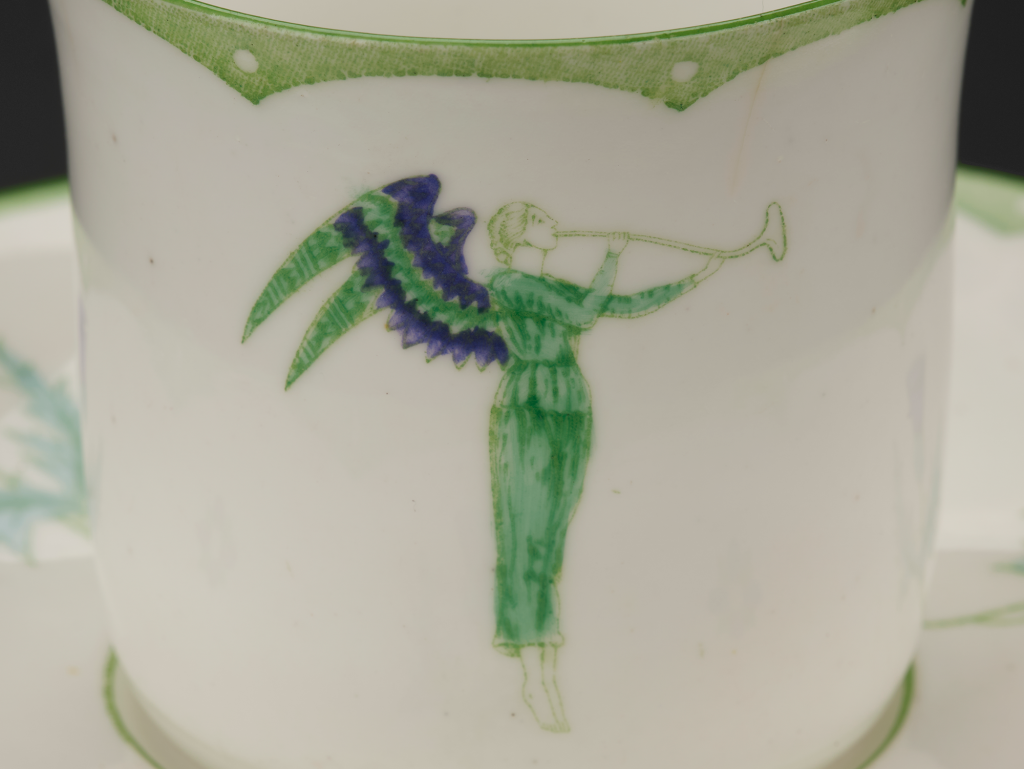 Image of a green and purple angel blowing a horn, on a cup.