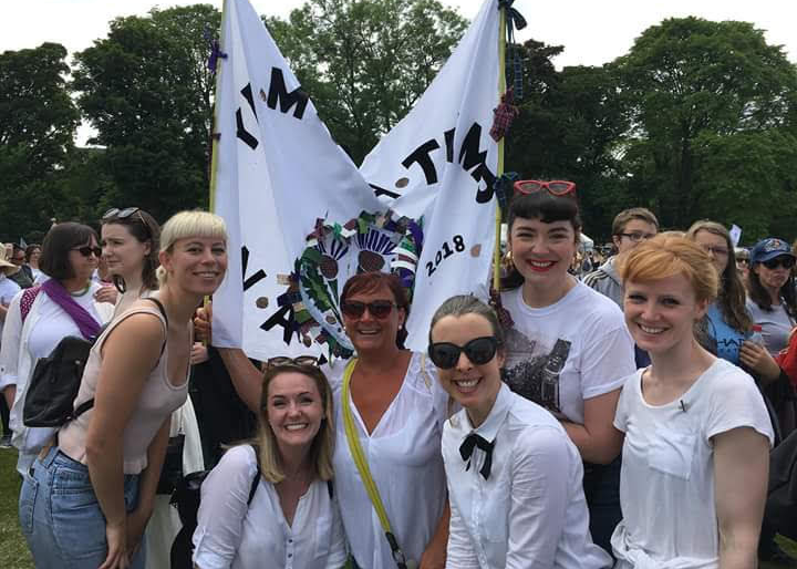Photo of a group of women wearing white posing with a banner.