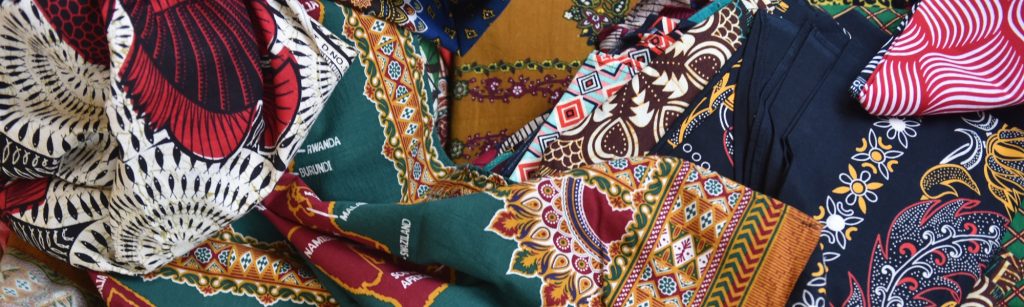Wide and narrow image of a pile of colourful fabrics with vibrant, naturalistic patterns.