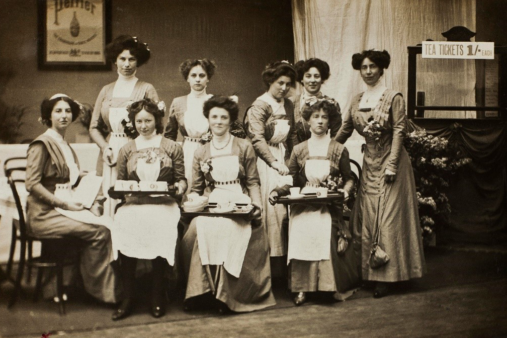 Sepia photo of women in 1909 with tea trays.