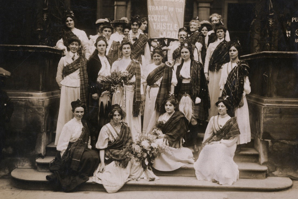 Sepia photo of women in 1908 standing on a set of steps and wearing sashes.