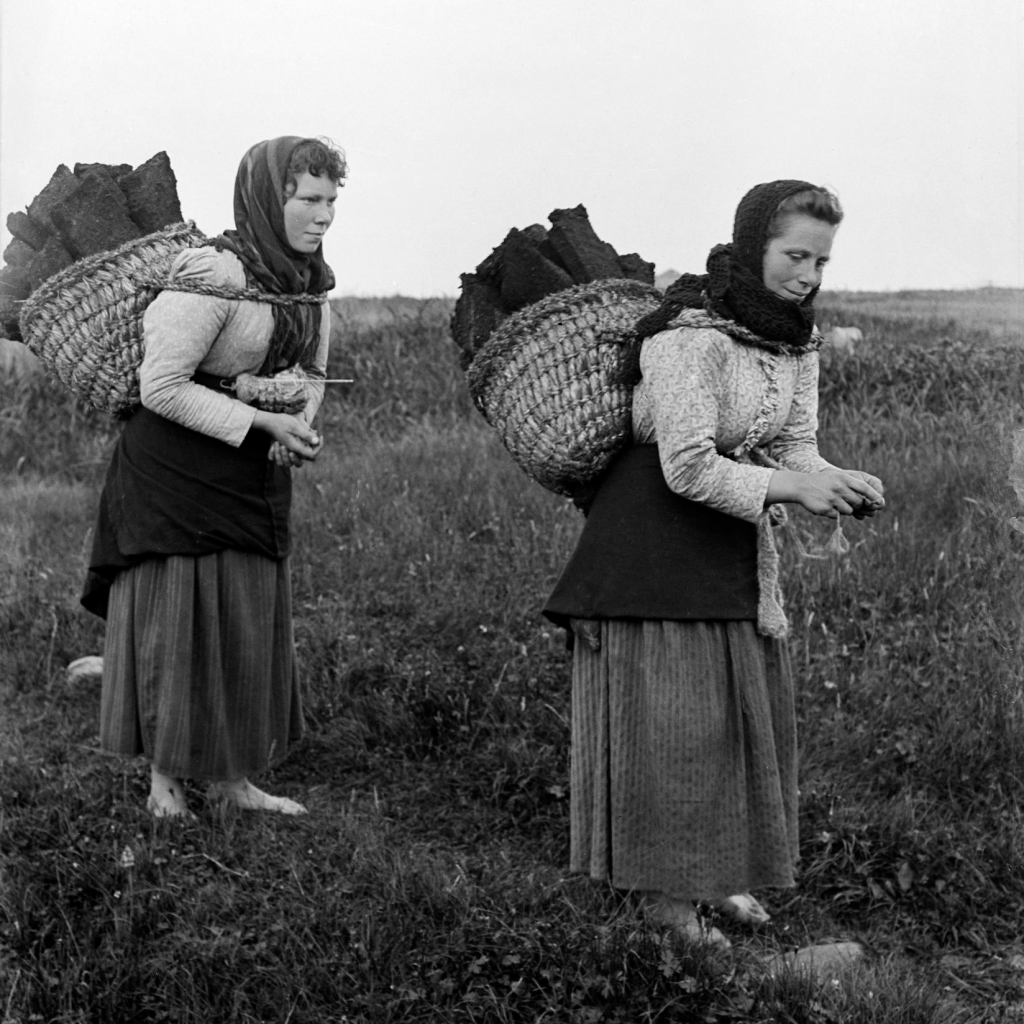 Black and white photo of women walking with baskets on their backs.