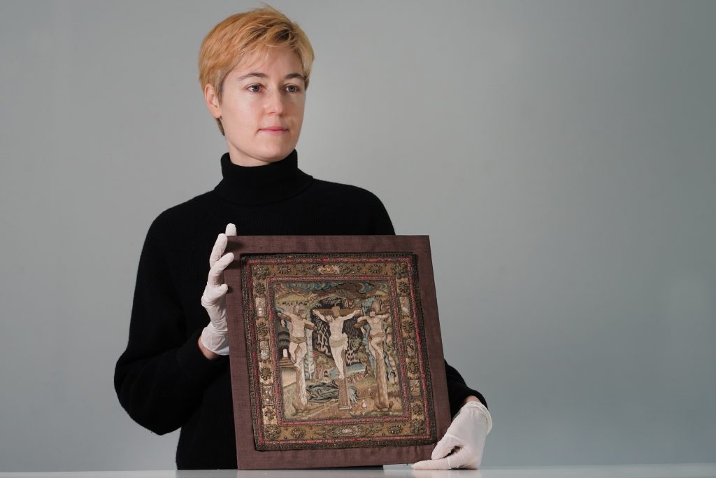 A woman holds the framed embroidery.
