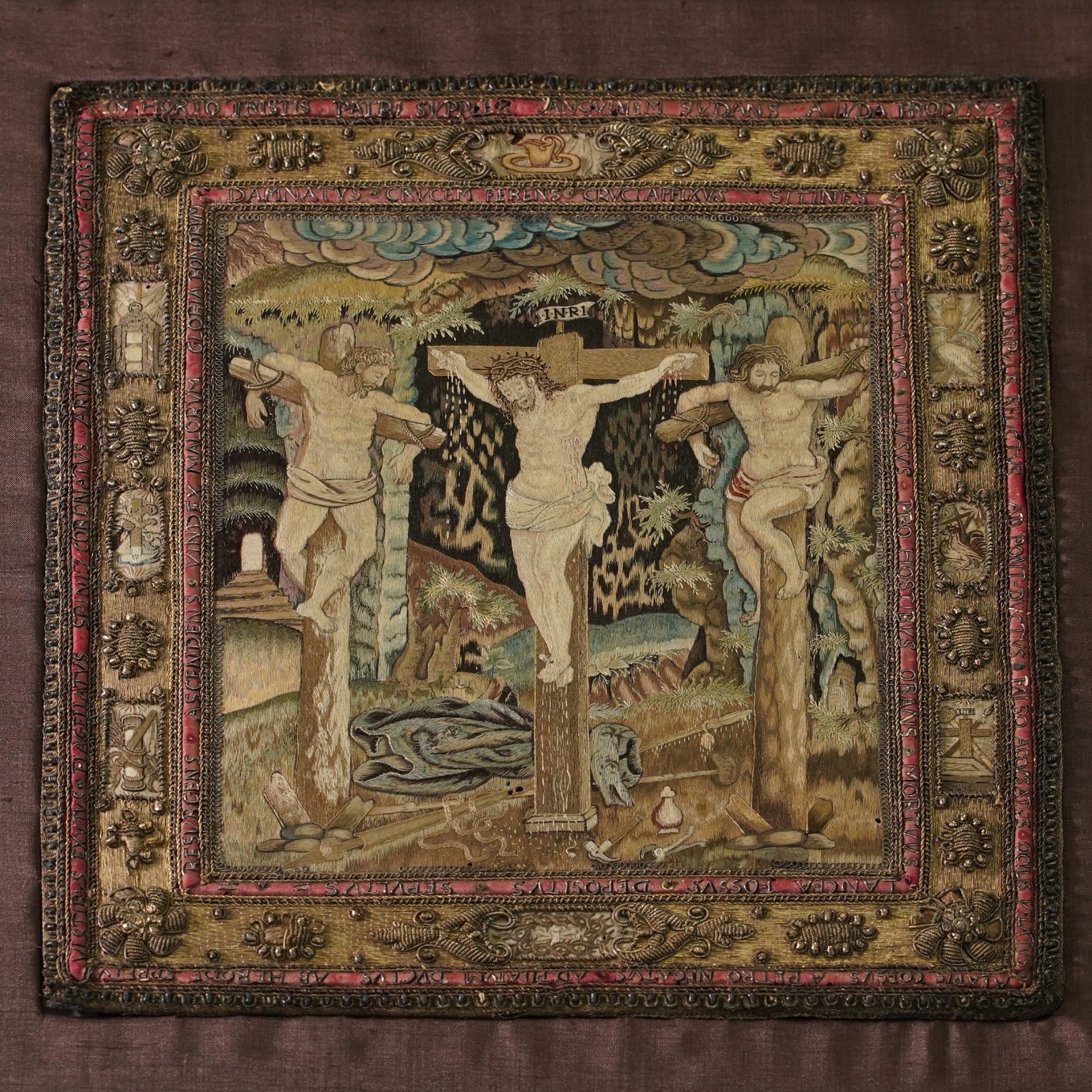 Embroidery created entirely in coloured silks. It shows Christ crucified on Golgotha, with the two thieves either side of him. Above is a dramatic sky; below are his discarded clothes, and the tools used to torture him.