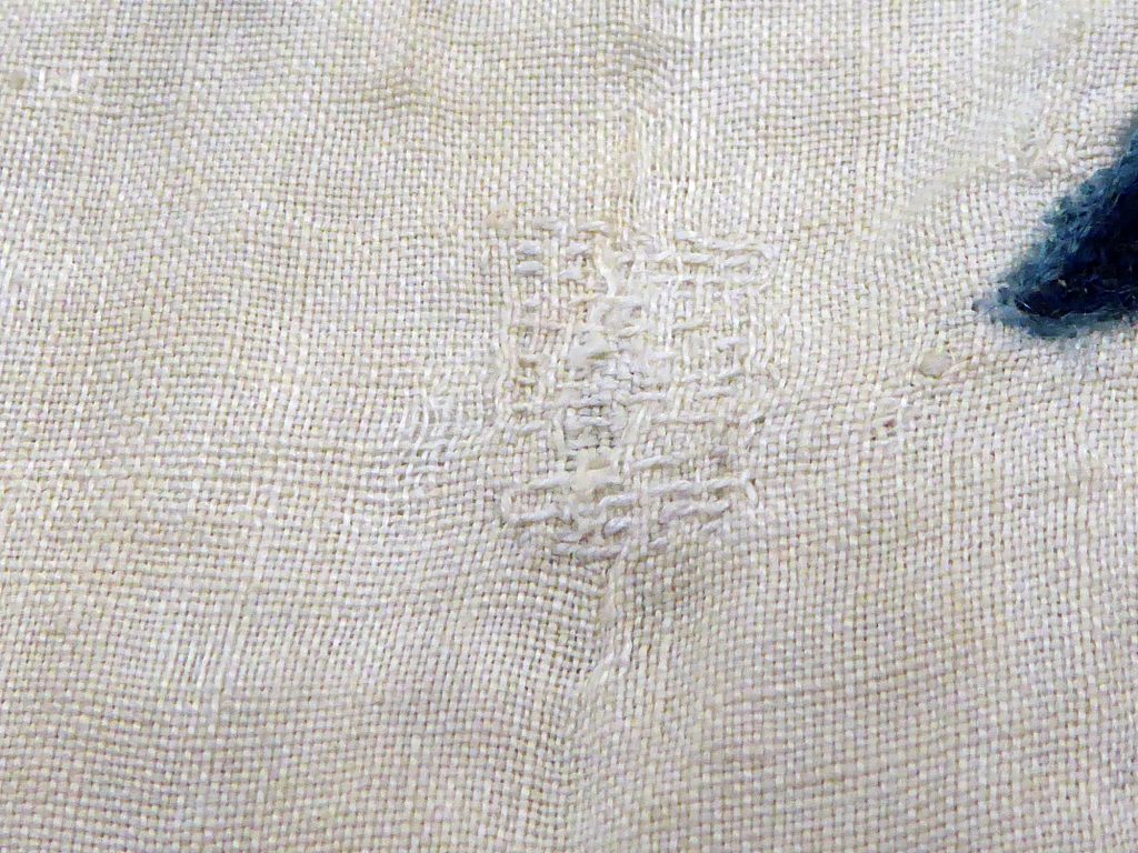 Close-up of white woven fabric that's been darned.