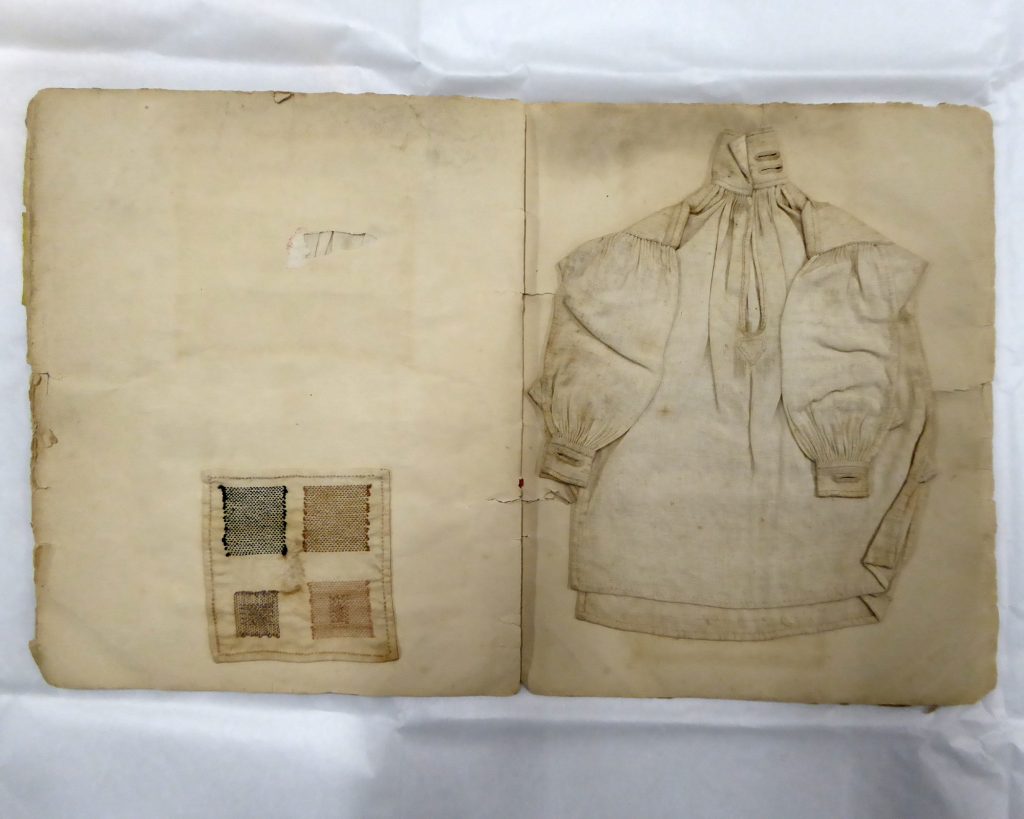 Photo of an opened book with a small shirt on one side and some darning examples on the other.
