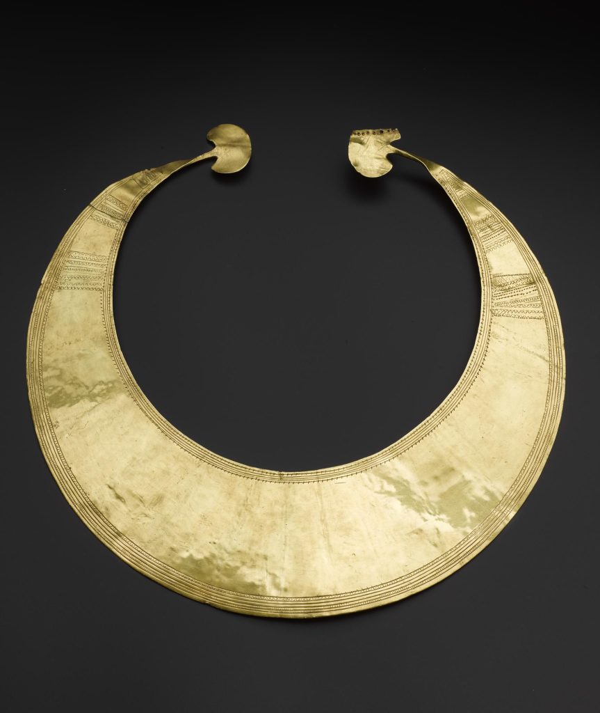 Flat, crescent-shaped gold object resembling a necklace on a black background.