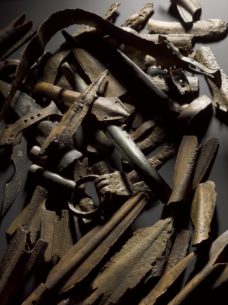 Large, chaotic pile of rusted metal objects including spearheads, buckles, bars and shards.