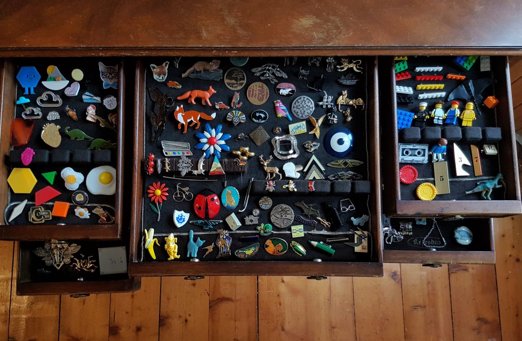 A cabinet viewed from the top with many drawers open, each one containing many colourful and varied brooches.