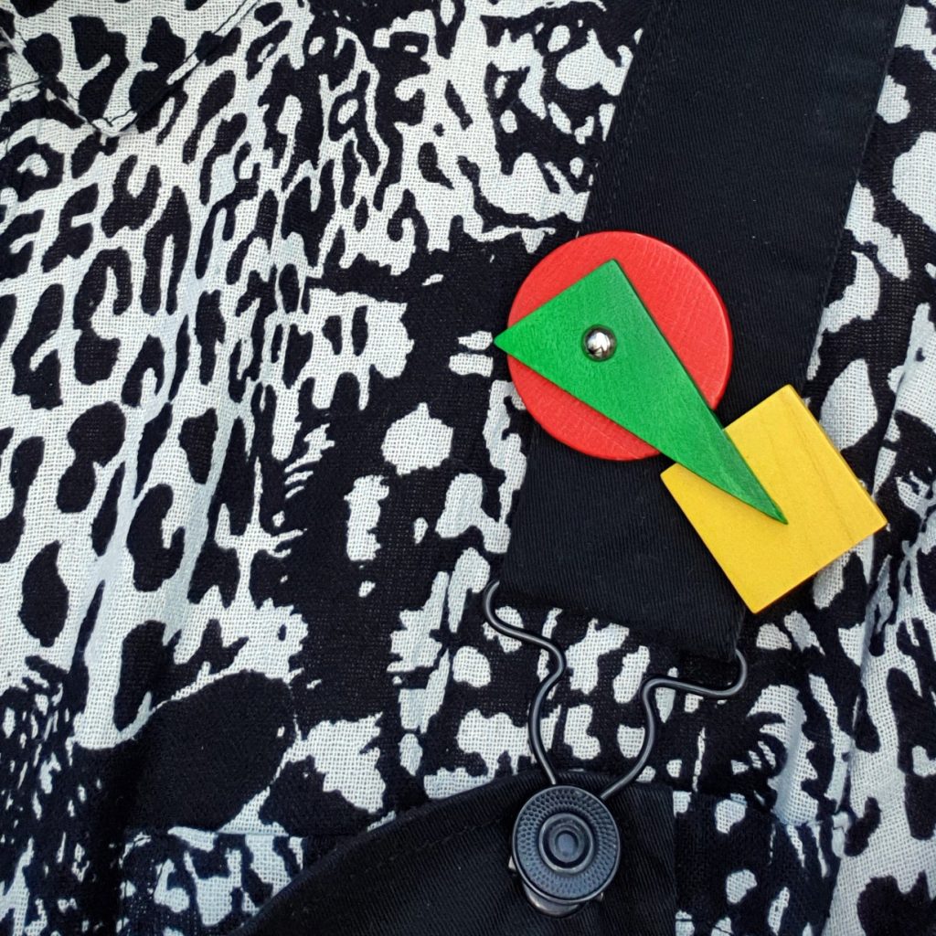 A colourful and abstract wooden shapes brooch against a white shirt.