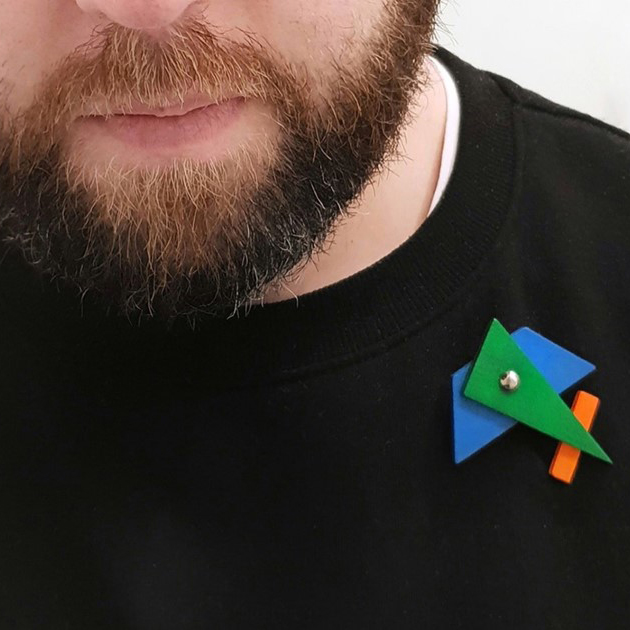 A colourful and abstract wooden shapes brooch against a black a jumper.