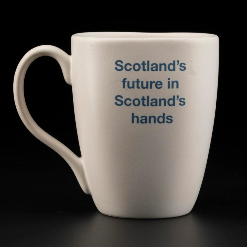 Simple white mug, tall but not overly so, with an earlobe-shaped handle and text in indigo blue reading 'Scotland's future in Scotland's hands'. 