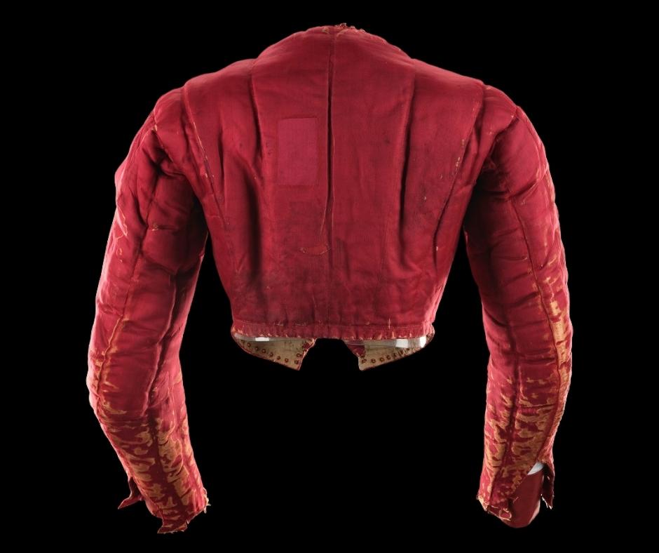 Back of the red and gold doublet against a black background. Elbows are slightly bent, and vertical lines emphasise pads across the back.