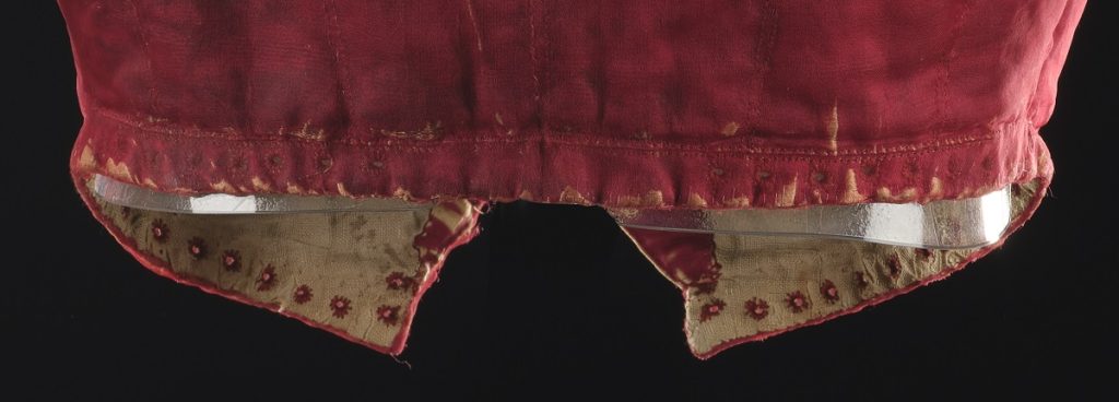 Closeup of the bottom of the doublet. Its inner front edges are lined with red dots and stitched eyelets.