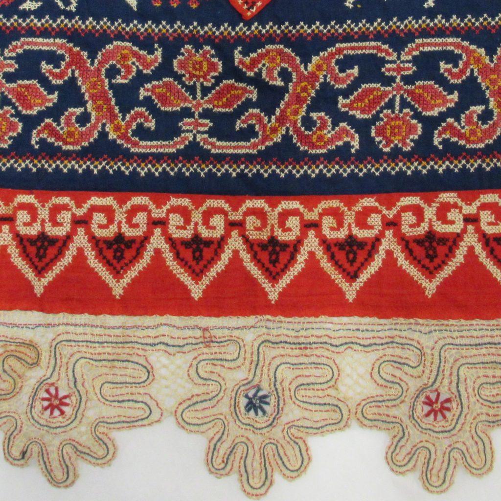 Close-up details of the woman’s dress and apron in dark blue cotton, embroidered with cotton threads in cross stitch.