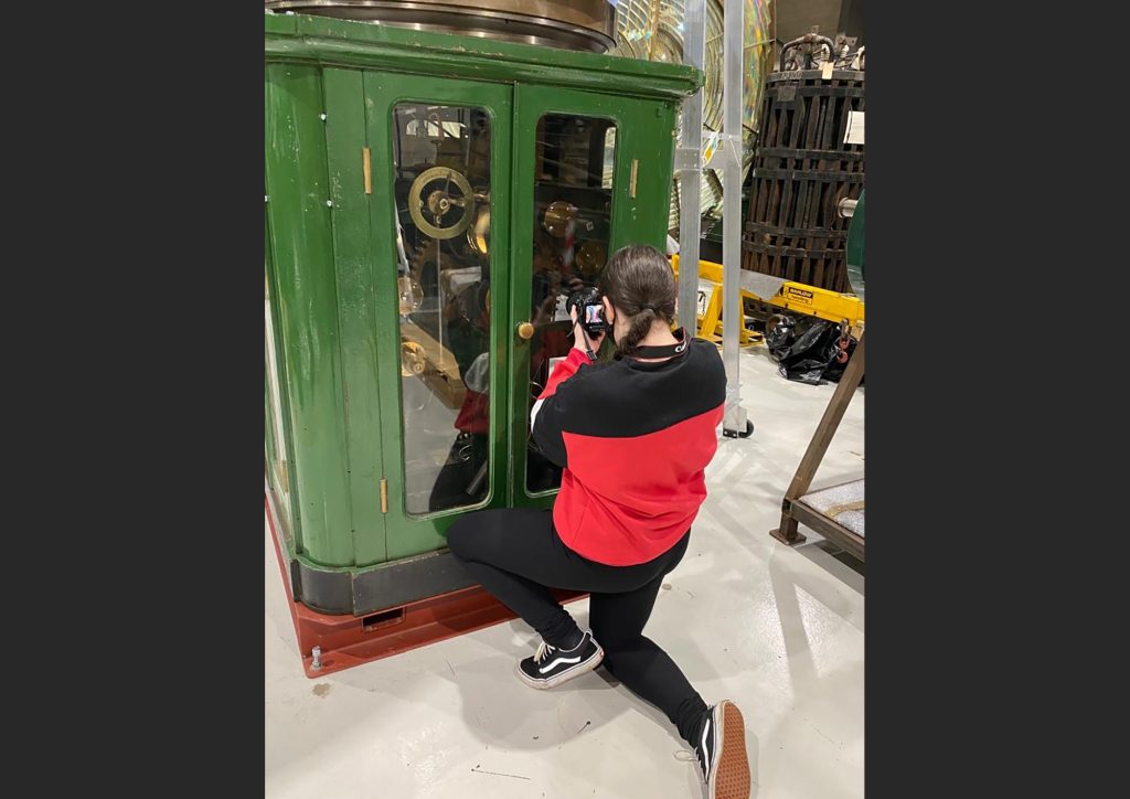 Colour photo of the rear view of a person taking a photo of a lighthouse lens mechanism.