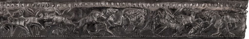 Very long, thin strip of metal presenting a rolled-out view of the decorations on the bowl's edge. A chaotic scene of big cats and predators hunting prey animals.