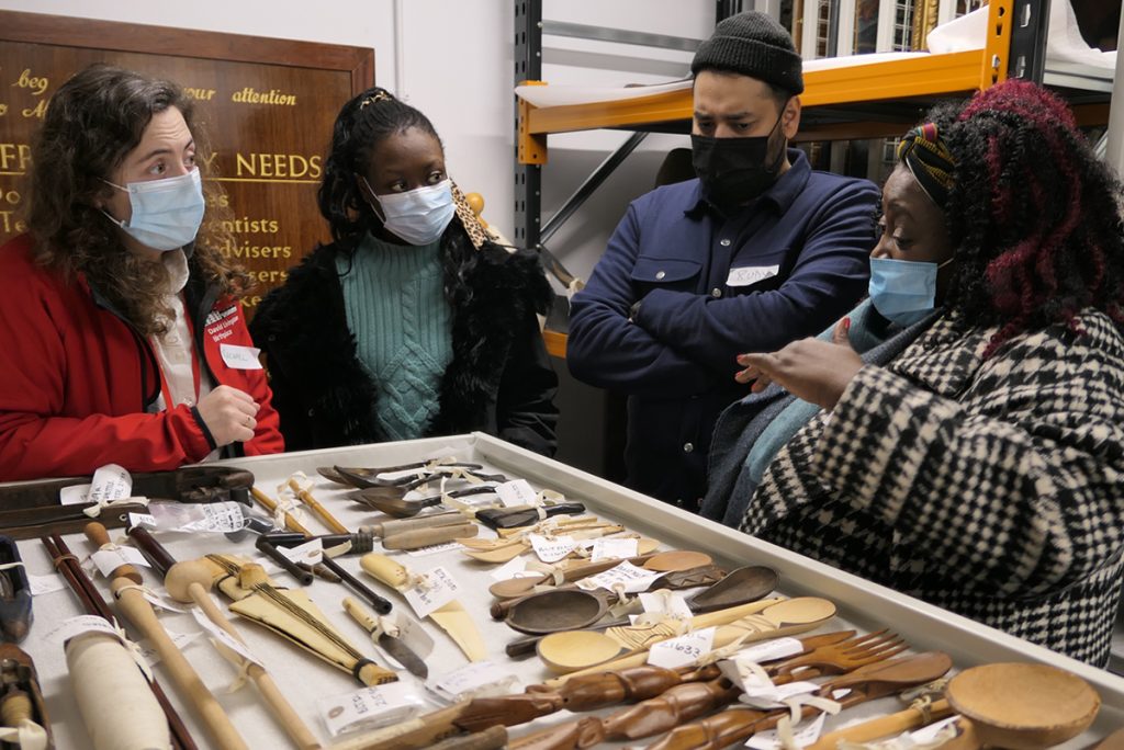 People standing around a drawer of wooden objects, one Black man, two Black women and one White woman, all wearing face masks.
