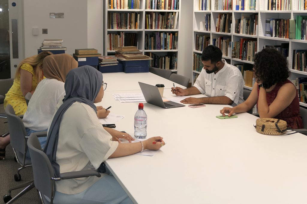 Young Brown people sitting around the table in a library space chatting and taking notes.