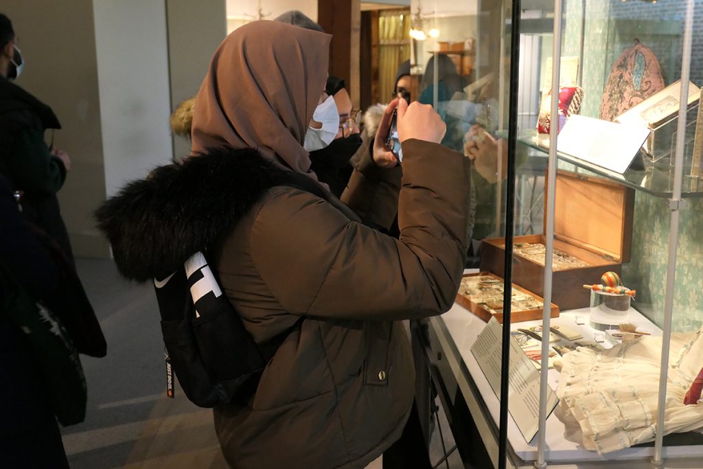A young Brown woman in a museum taking a photo of a display.