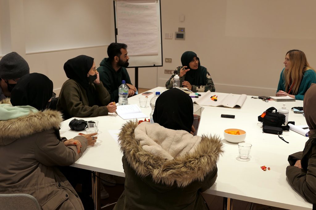 A group of young Brown people sit around a table in discussion.