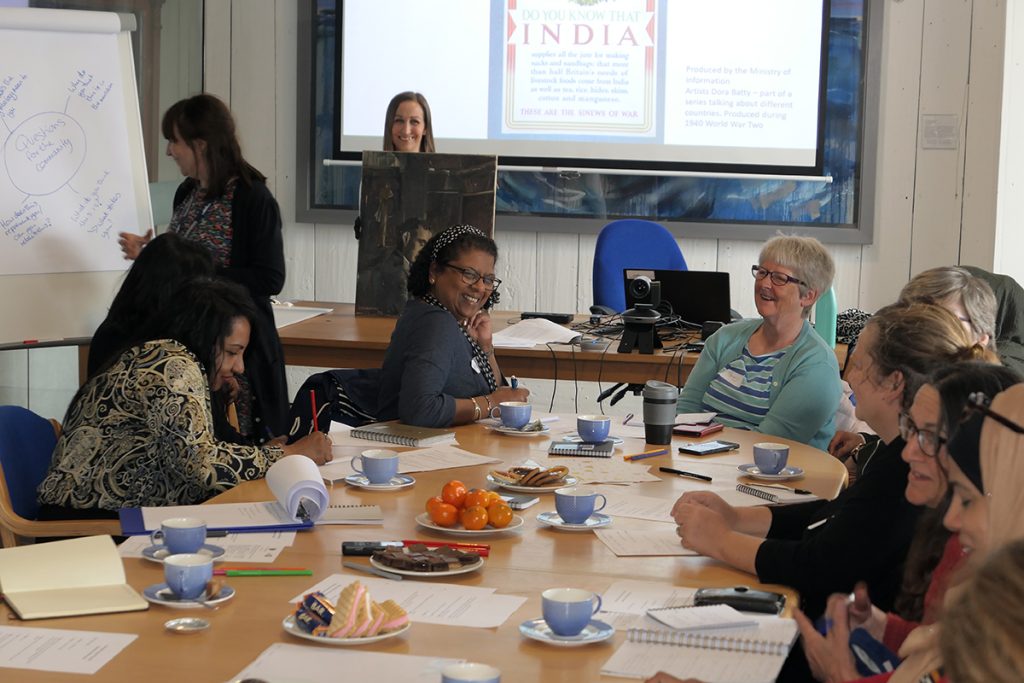 A workshop with South Asian and White women around a table chatting and smiling.